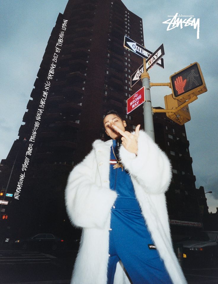 a woman in a white fur coat standing next to a street sign and traffic light