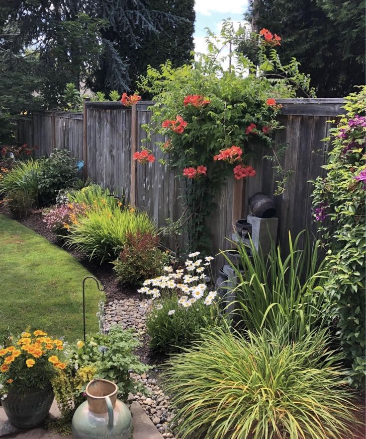 a garden with lots of flowers and plants in the back yard, along with a wooden fence