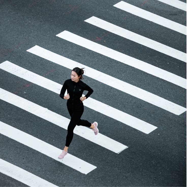 a woman running across a crosswalk in the middle of an intersection with white lines