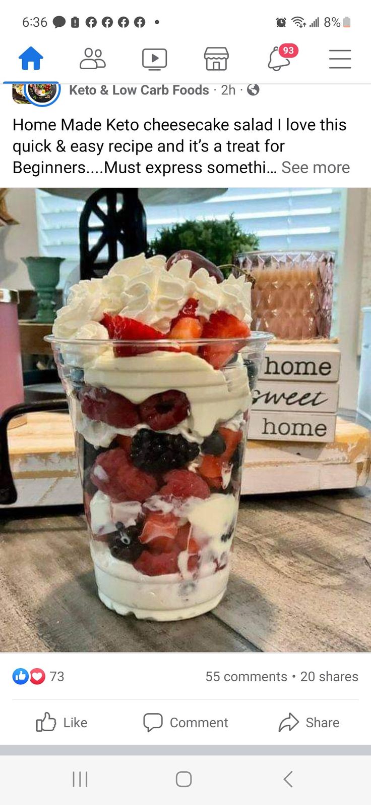 a cup filled with fruit and whipped cream on top of a wooden table next to a window