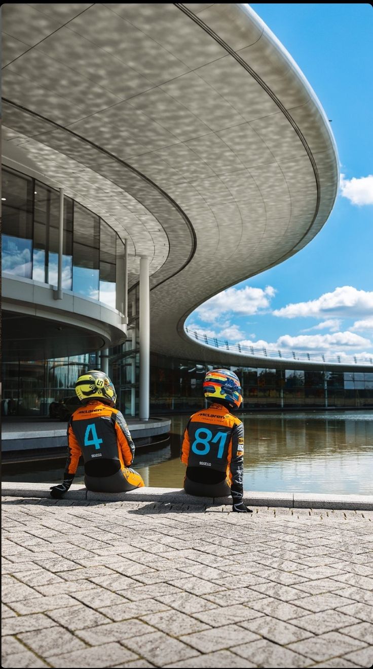 two people sitting next to each other in front of a building with a large body of water