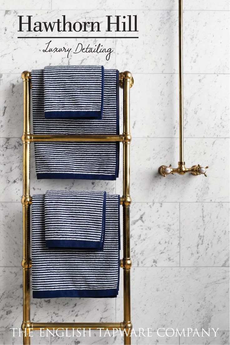 two towels are hanging on a towel rack next to a marble tiled wall and gold faucet