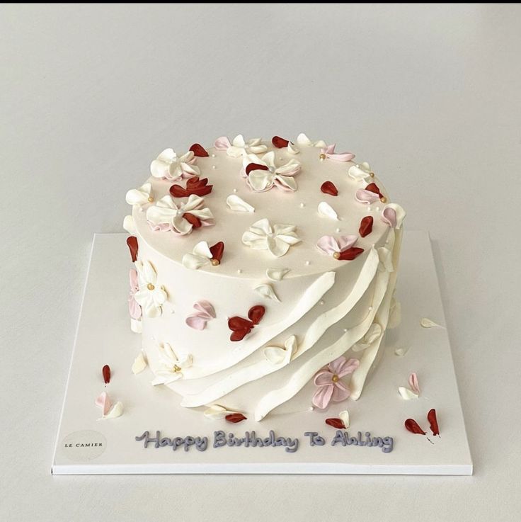 a birthday cake with white frosting and pink flowers on top is sitting on a card