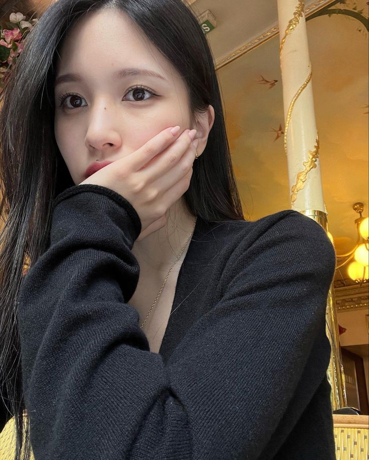 a woman with long black hair is holding her hands to her face and looking at the camera