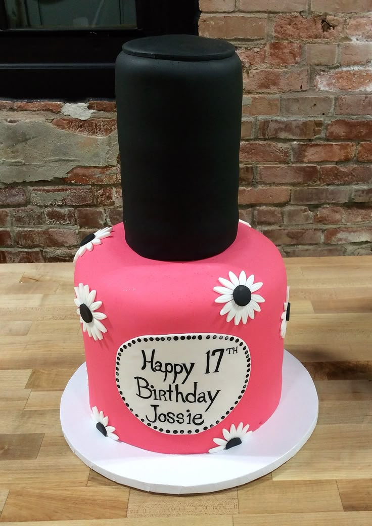 a pink birthday cake decorated with daisies on a table next to a brick wall