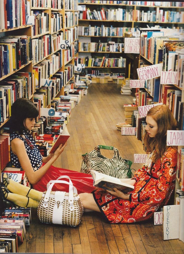 two women sitting on the floor in front of bookshelves and holding purses