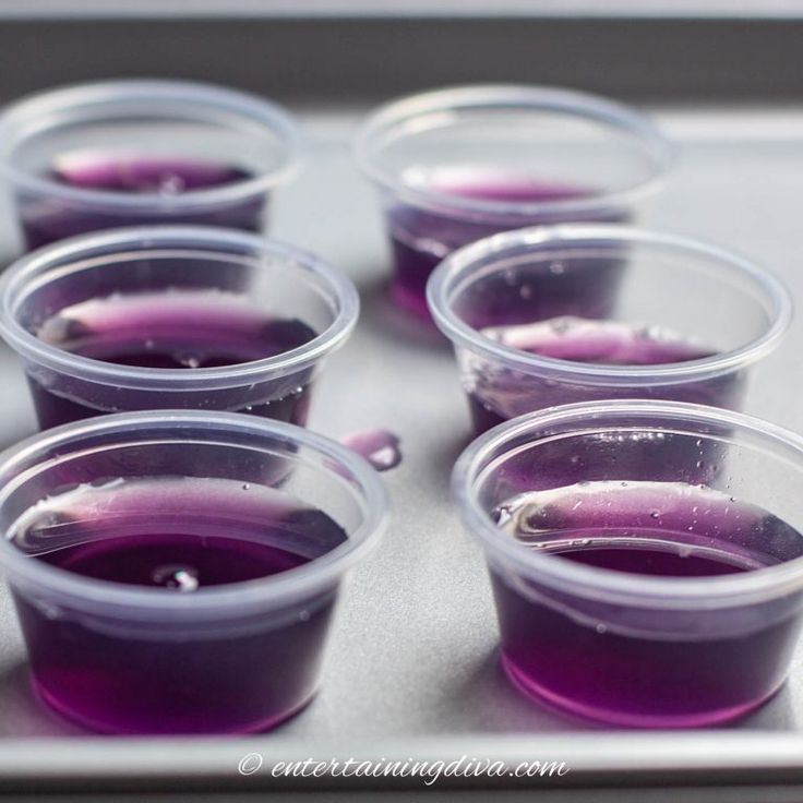 purple liquid in plastic cups sitting on top of a metal tray