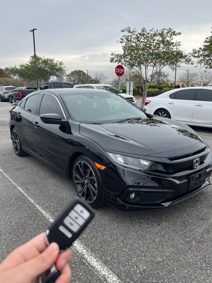 a person holding a car key in front of a black honda civic hatch parked in a parking lot