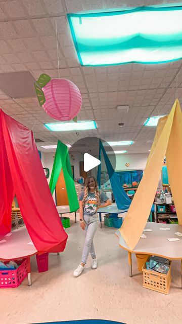 a girl is standing in the middle of a room with colorful tents hanging from the ceiling