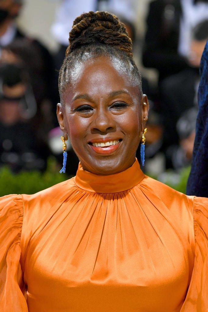 a woman in an orange dress smiles at the camera while wearing large blue earrings on her head