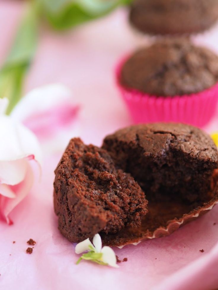 three chocolate muffins on a pink plate with flowers and petals around them, one half eaten