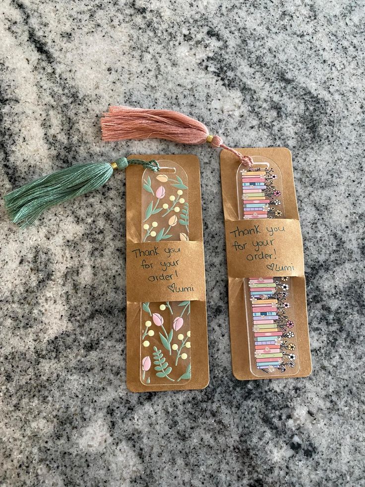 two bookmarks with tassels on them sitting on a marble counter top next to each other