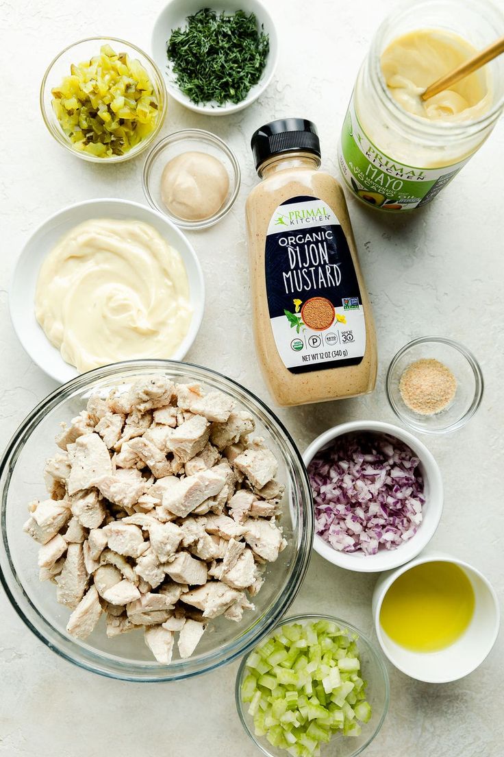 ingredients to make chicken salad laid out on a white counter top, including onions, celery, mustard and dressing