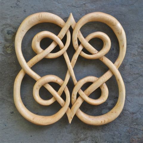 an intricately carved wooden object on a stone surface with knots in the middle and two circles at the center