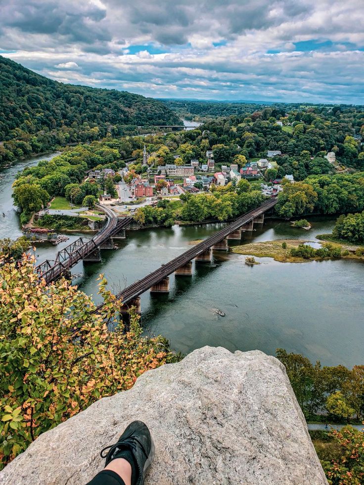 a person's feet on the edge of a cliff overlooking a river and bridge