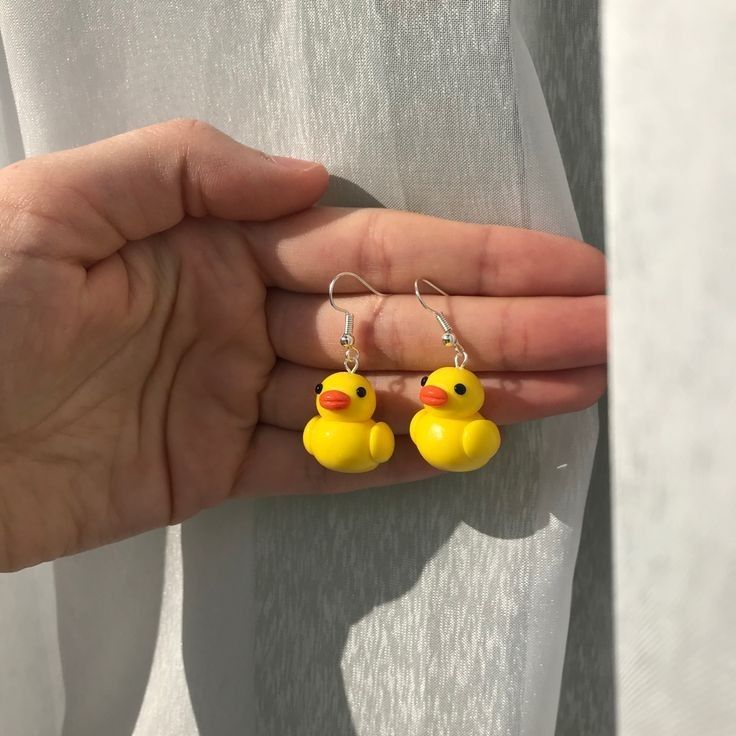 a person holding two small yellow rubber ducks in their left hand while wearing matching earrings