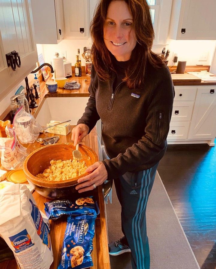 a woman standing in a kitchen holding a bowl filled with food and smiling at the camera