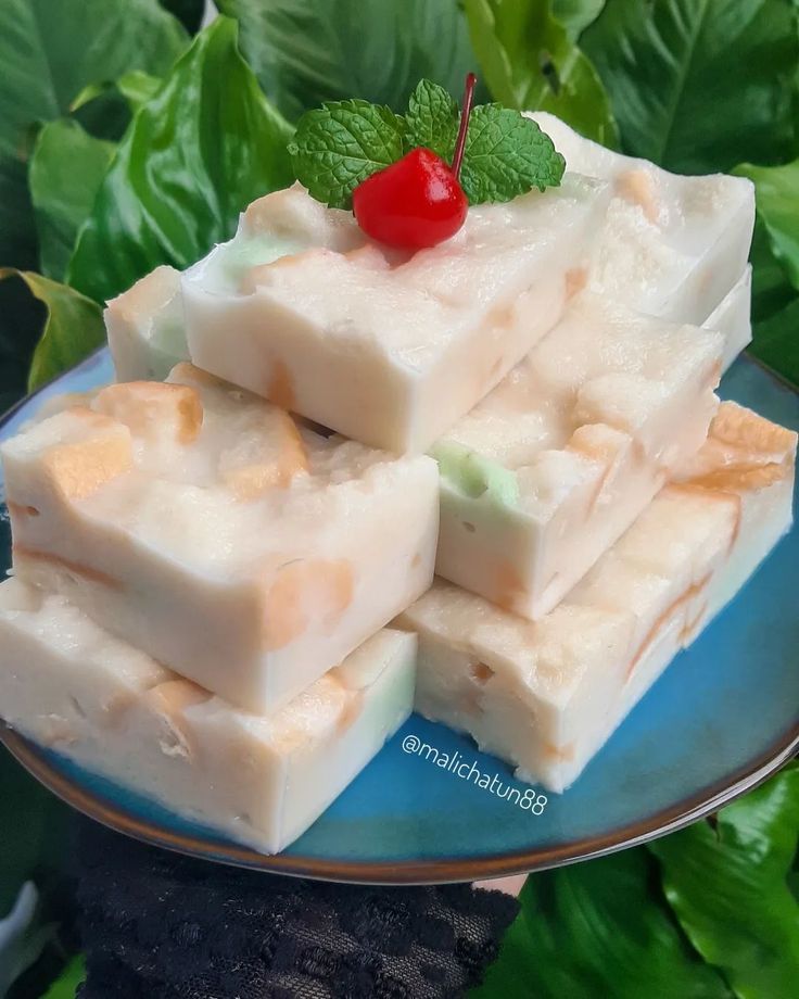 a blue plate topped with pieces of white fudge next to green leaves and a cherry