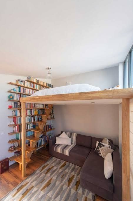 a living room with a couch, bookshelf and stairs in the wall next to it