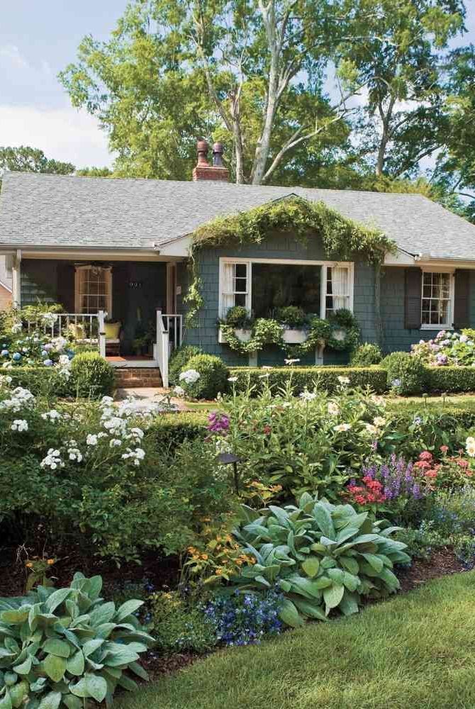 a house with lots of flowers in front of it and bushes around the front yard