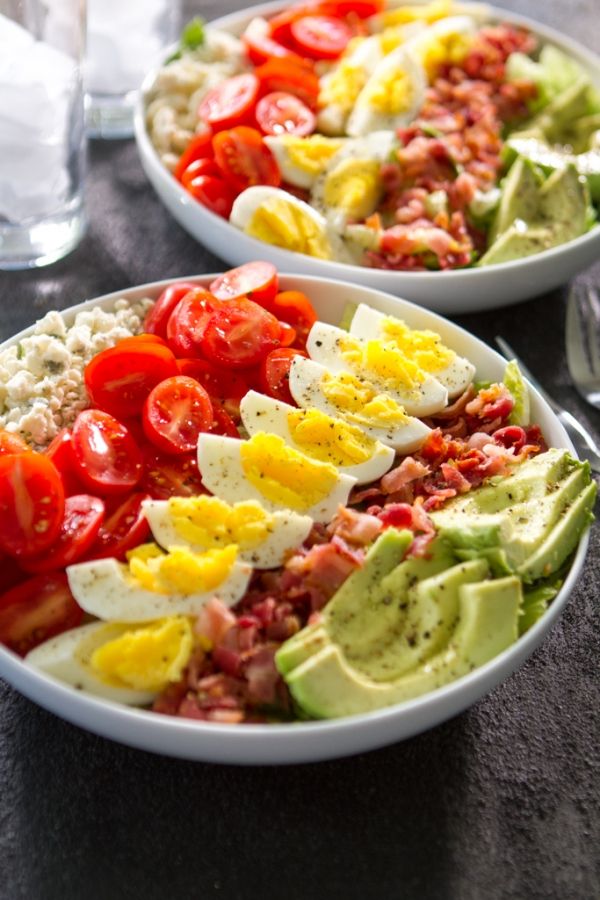 two white bowls filled with different types of food on top of a black table next to silverware