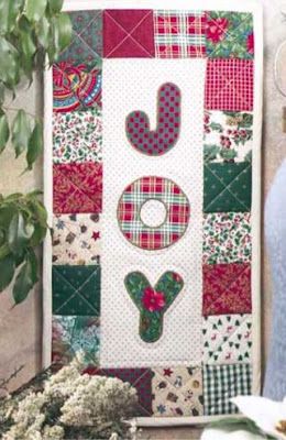 a quilted wall hanging next to a potted plant and vase with flowers in it