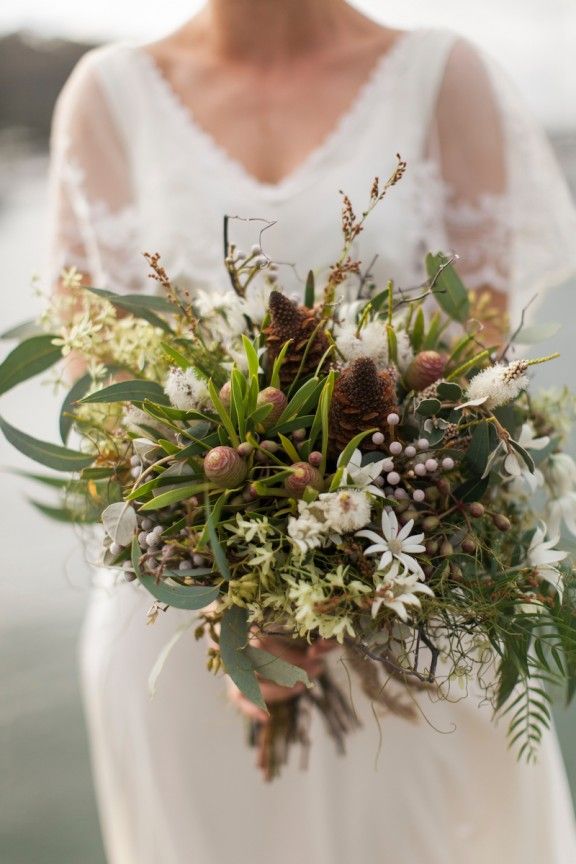 a bride holding a bouquet of flowers and greenery in her hands with water in the background