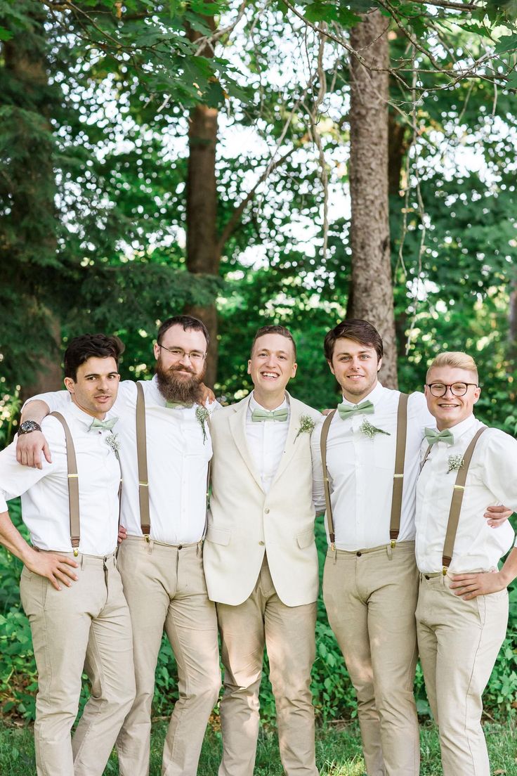 a group of men standing next to each other wearing suspenders and bow ties in front of trees