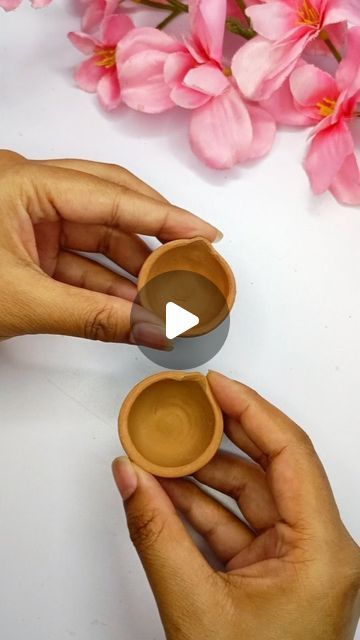 two hands holding small cups on top of a white table with pink flowers in the background