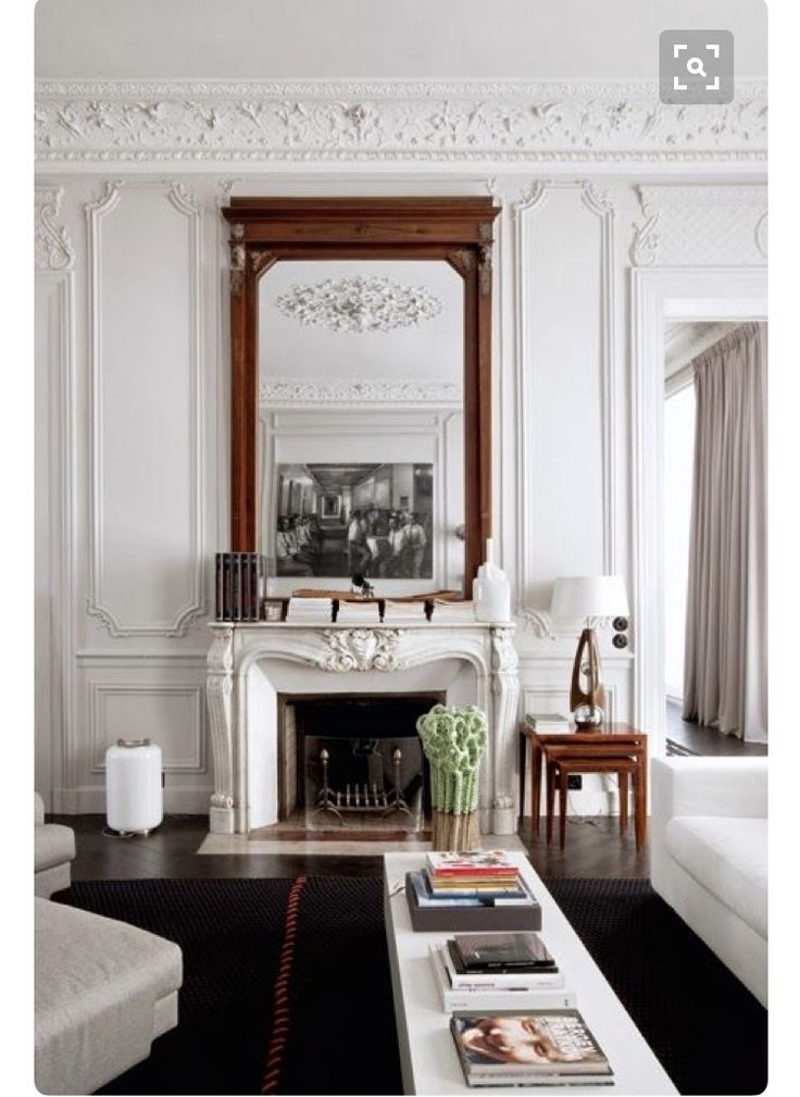 a living room with white furniture and a large mirror above the fireplace in front of it