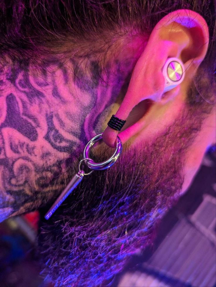 a pair of ear piercings on top of a man's head with purple light