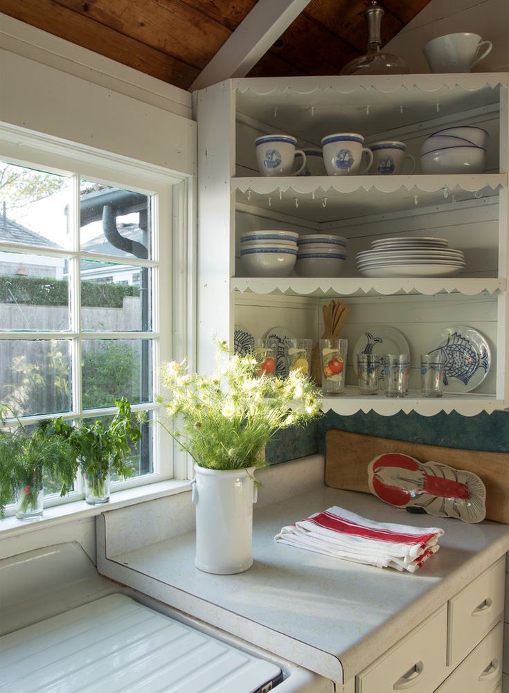 a kitchen with white cabinets and shelves filled with dishes, plates and flowers in a vase