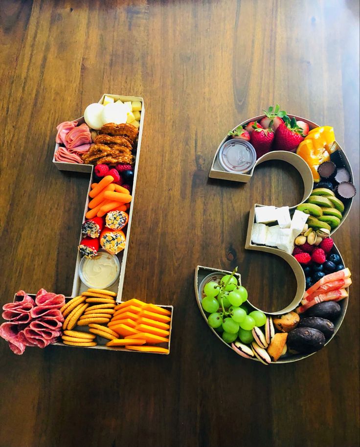 the number five made out of food is displayed on a wooden table with grapes, carrots, cucumbers and other fruits