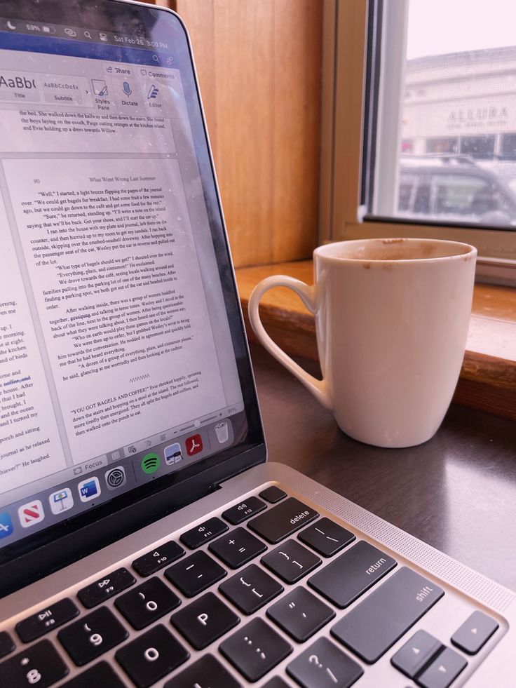 an open laptop computer sitting on top of a wooden desk next to a cup of coffee