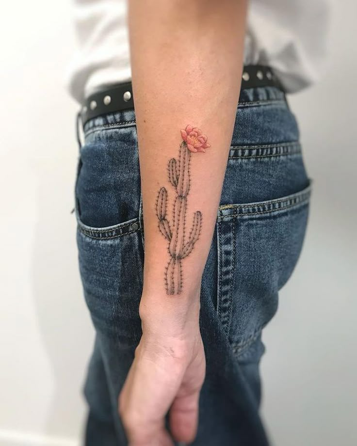 a small cactus tattoo on the left forearm and hand, with a pink flower in it