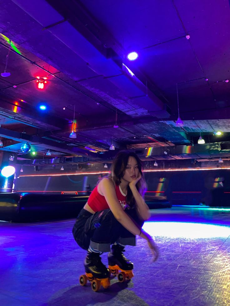 a woman riding a skateboard on top of an indoor skating rink in front of colorful lights