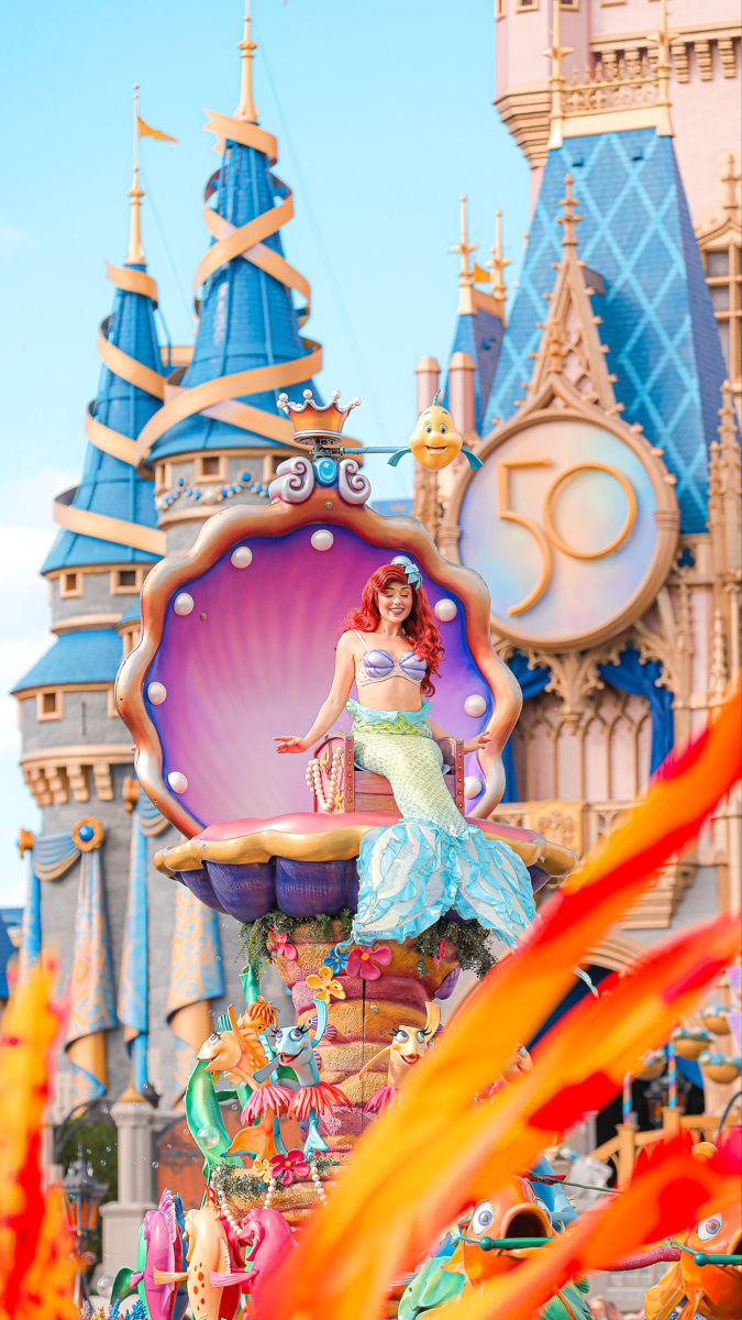 a woman in a mermaid costume standing on top of a float at the disney world parade