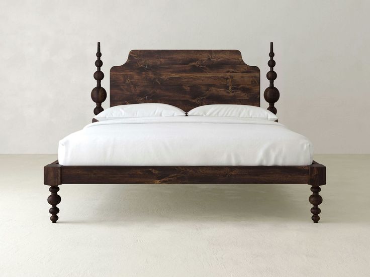 a wooden bed frame with white sheets and pillows on top of it, in front of a plain wall