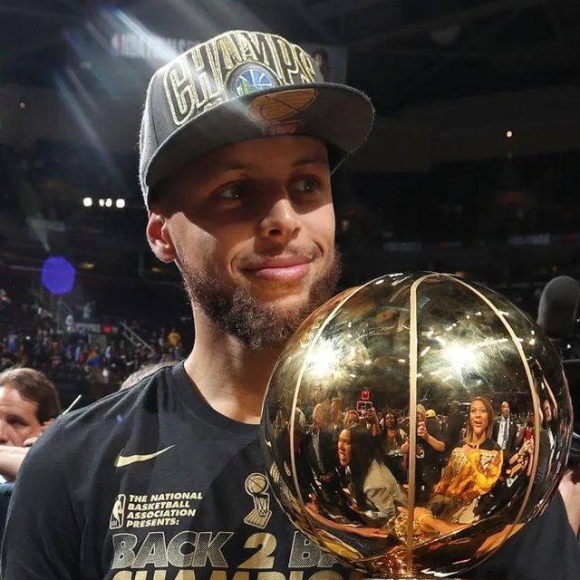 a man holding up a basketball trophy in front of a group of people at a game