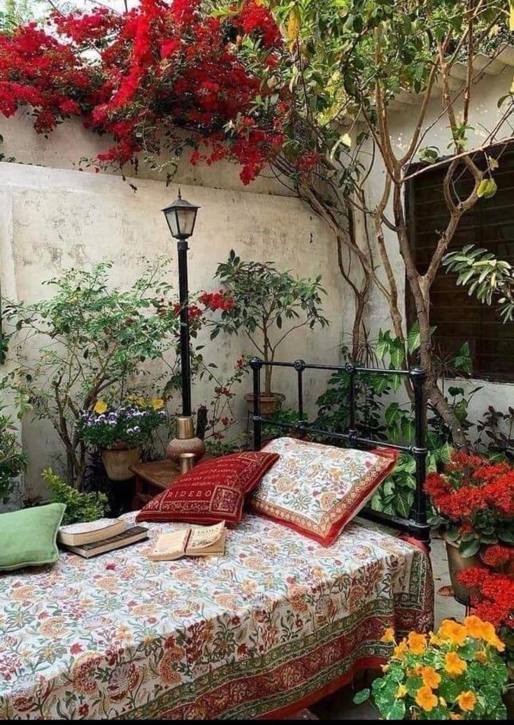 a bed sitting under a tree filled with flowers next to a lamp and potted plants