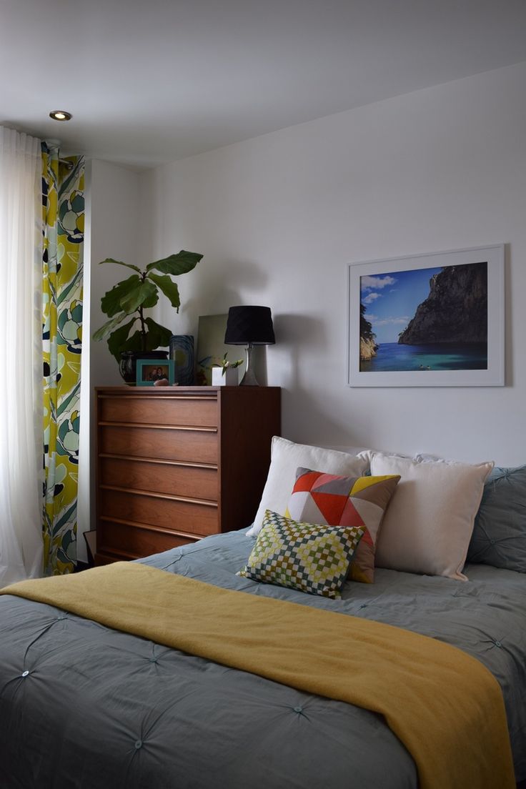 a bed sitting next to a window in a bedroom under a painting on the wall