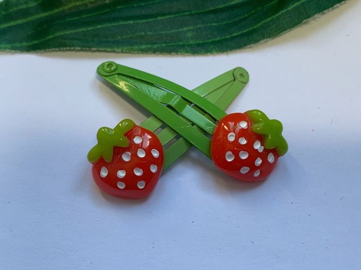 two red strawberries sitting on top of a green piece of paper next to a leaf