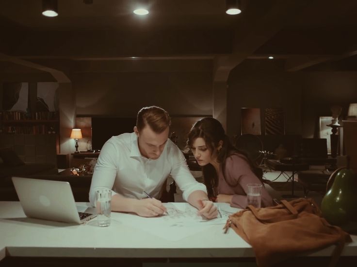 a man and woman sitting at a table looking at papers