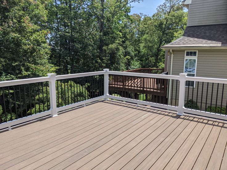 a wooden deck with white railings next to a house and trees in the background