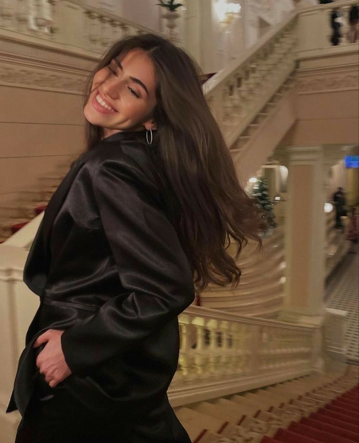 a woman standing in front of a set of stairs wearing a black jacket and skirt