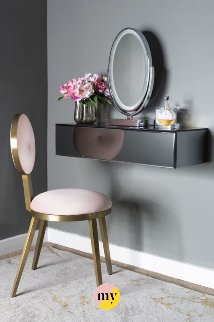 a vanity with a mirror, stool and flowers on the table in front of it