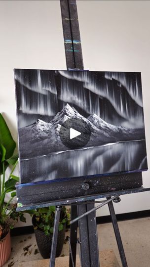 an easel with a painting on it in front of a potted plant