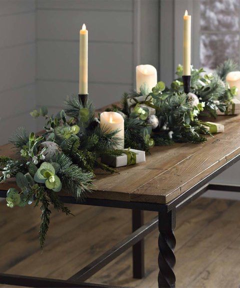 a wooden table topped with candles and greenery