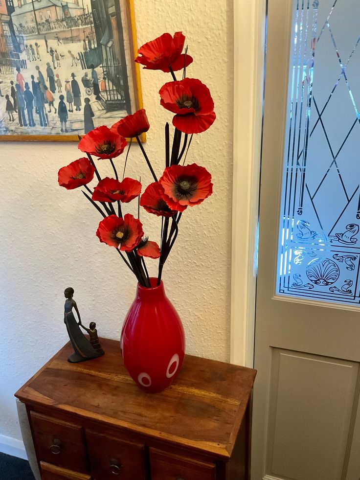 a red vase filled with flowers sitting on top of a wooden table next to a door