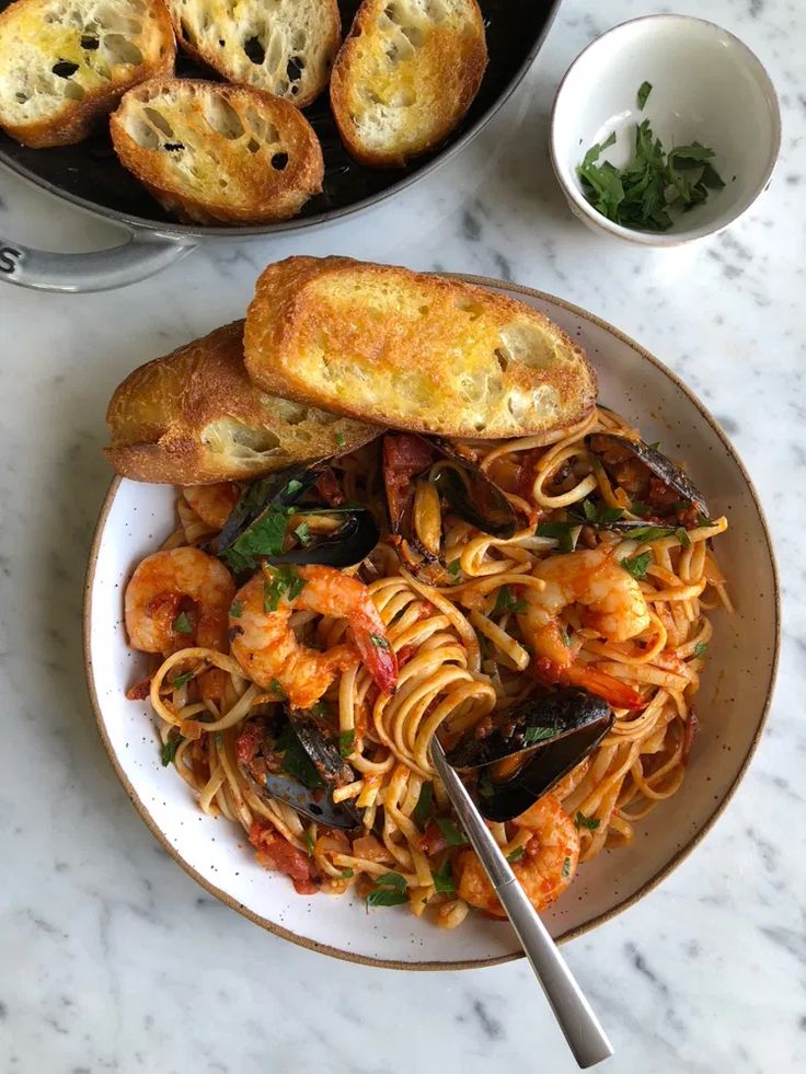 a plate of pasta with shrimp and garlic bread on the side, next to a bowl of parmesan bread